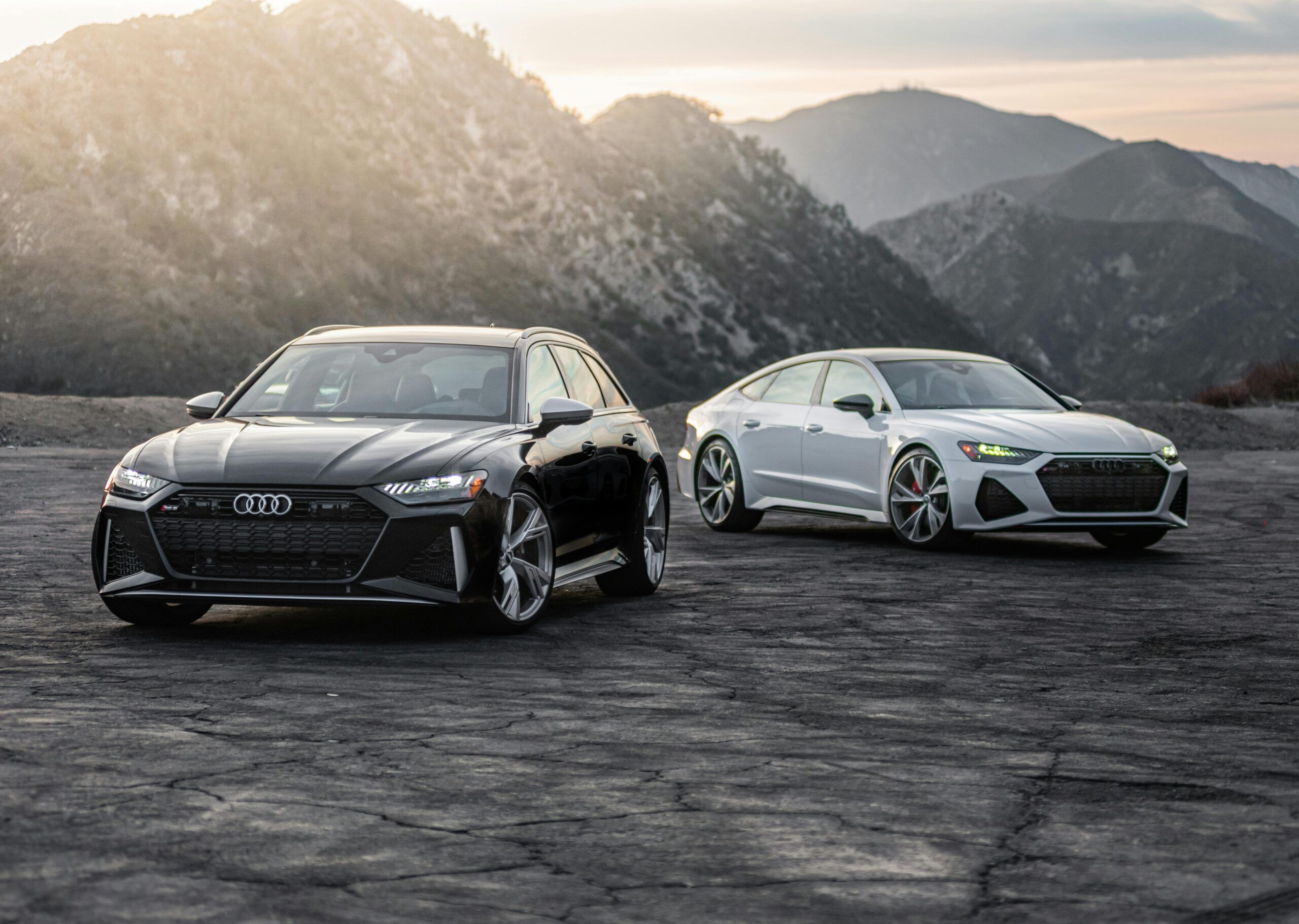 Two luxury Audi RS models parked on a scenic mountain road at sunset.